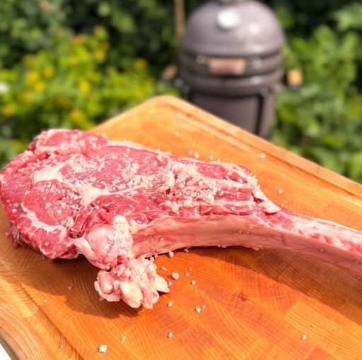 Tomahawk steak op de snijplank, kamado op de achtergrond